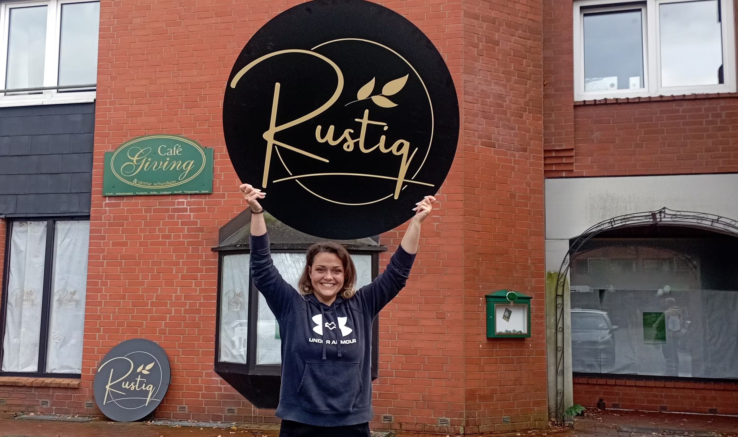 Inhaberin Andreea Varga mit dem goldenen Rustiq-Logo vor dem Café in Wahlstedt